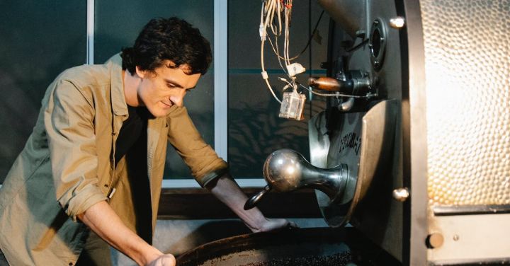 Automatic Train Control - Side view of pensive male standing near modern professional coffee roasting machine with heap of coffee beans in rotating drum