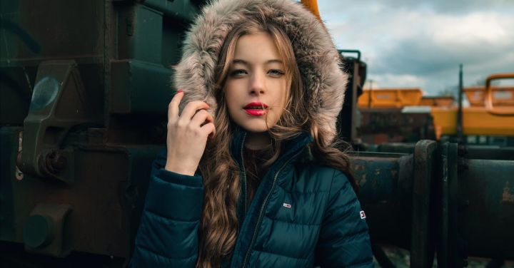 Model Railway - Serious young woman in warm clothes standing on railway near train and looking at camera