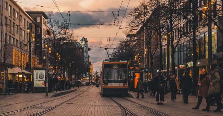 Winter Railway - Modern tram on railroad with people walking in old town with low rise buildings in cold twilight