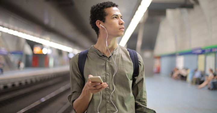 Railroad Exhibitions - Young ethnic man in earbuds listening to music while waiting for transport at contemporary subway station