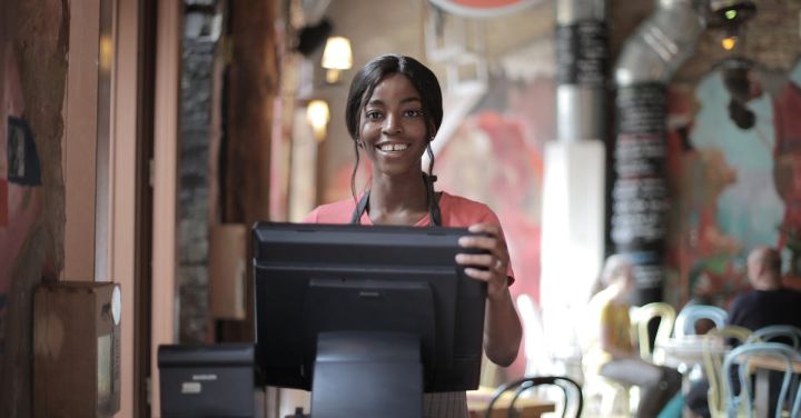 Orient Express - Positive young woman in uniform smiling while standing at counter desk in cafe